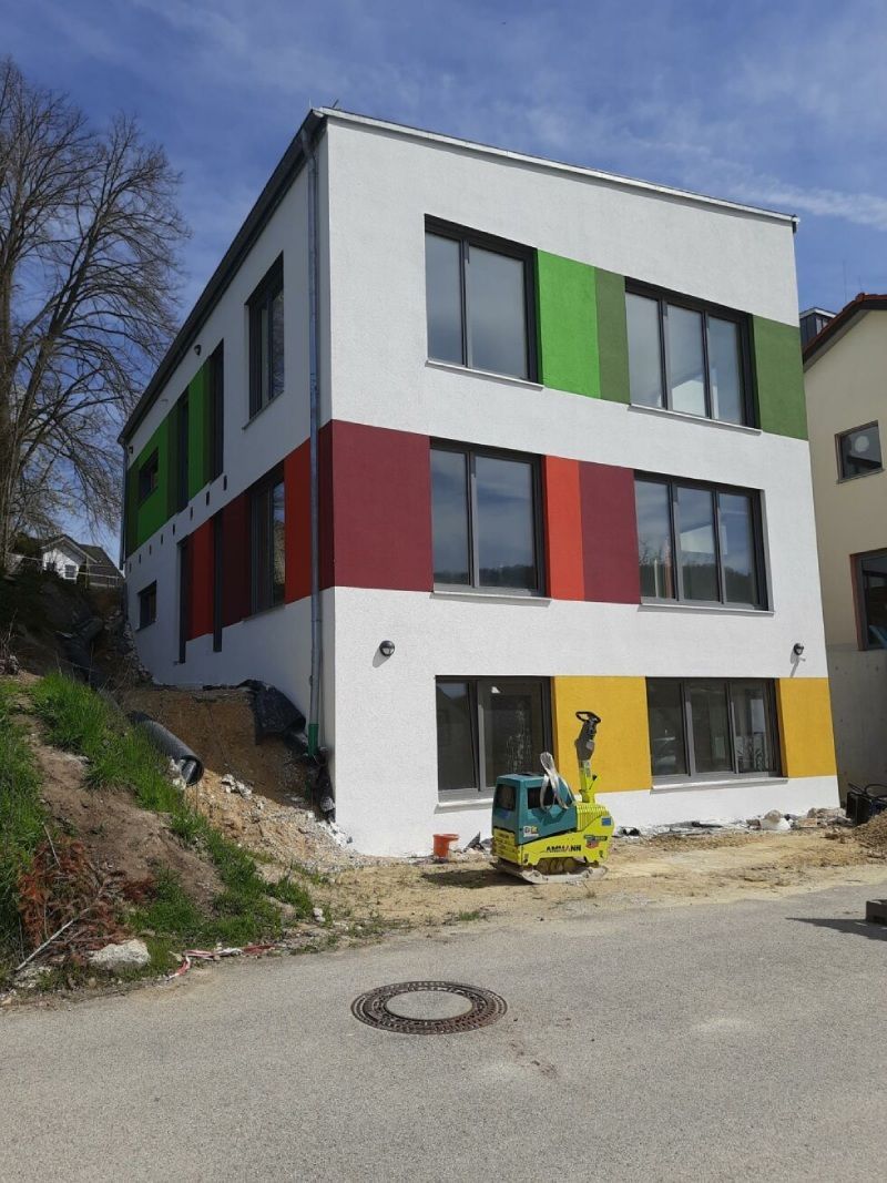 Modernes weißes Gebäude mit farbigen Fensterpaneelen an einer Hangstraße unter blauem Himmel