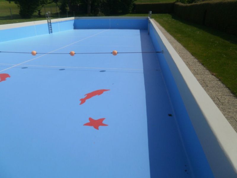 Leeres Schwimmbecken mit blauer Auskleidung, roten Fisch- und Seesternmotiven und orangefarbenen Schwimmkörpern am anderen Ende