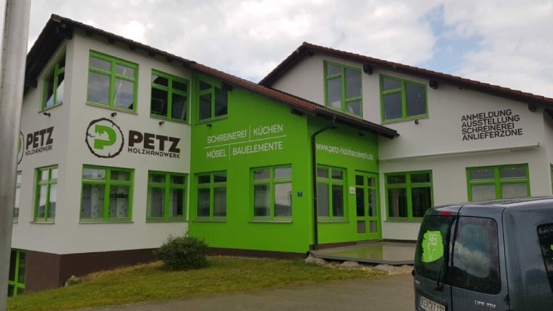 Ein hellgrünes PETZ-Geschäftsgebäude mit weißer Fassade und geparktem Fahrzeug davor.