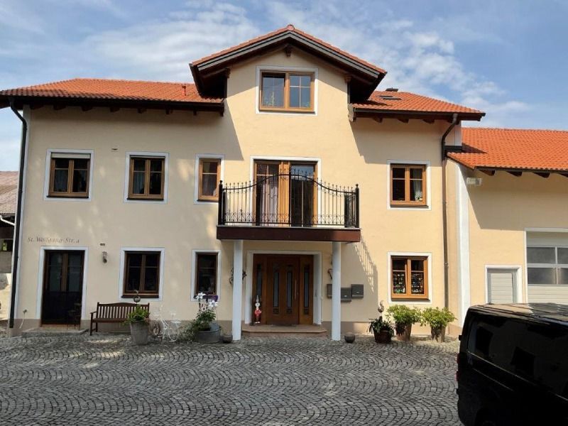 Beiges zweistöckiges Haus mit rotem Ziegeldach, Balkon und gepflasterter Auffahrt unter klarem Himmel