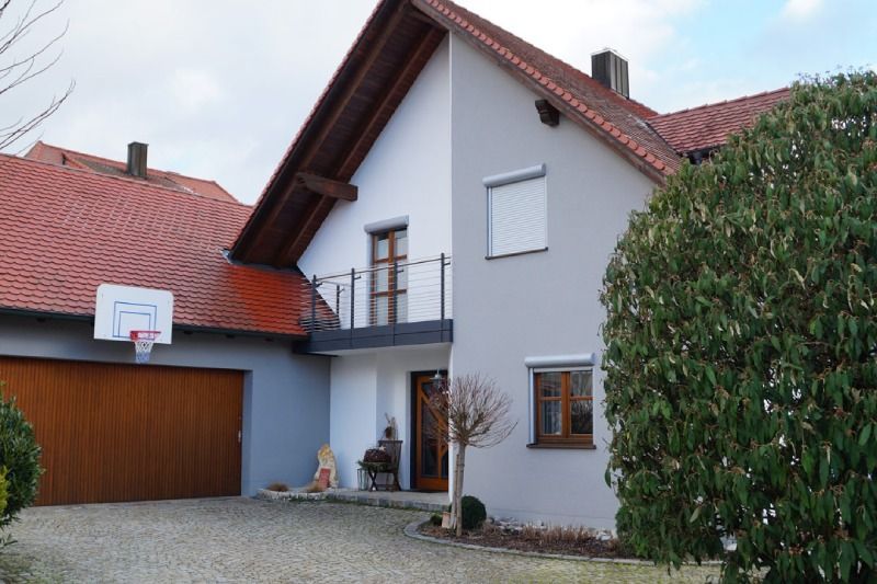 Zweistöckiges Haus mit rotem Ziegeldach, Garage, Basketballkorb und einer Person, die am Eingang steht