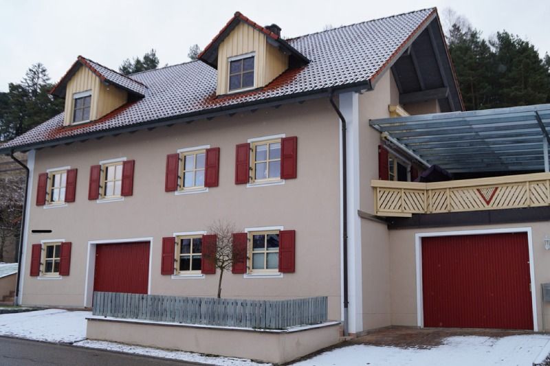 Schneebedecktes Haus mit roten Fensterläden, Dachgauben und einem roten Garagentor