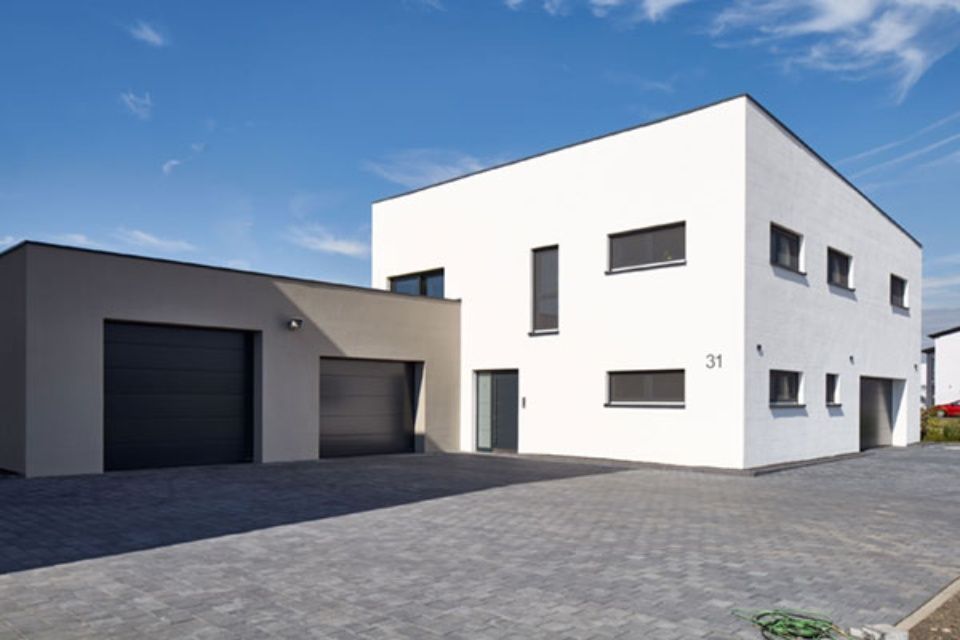 Modernes weißes Haus mit dunkler Garage und gepflasterter Auffahrt unter blauem Himmel