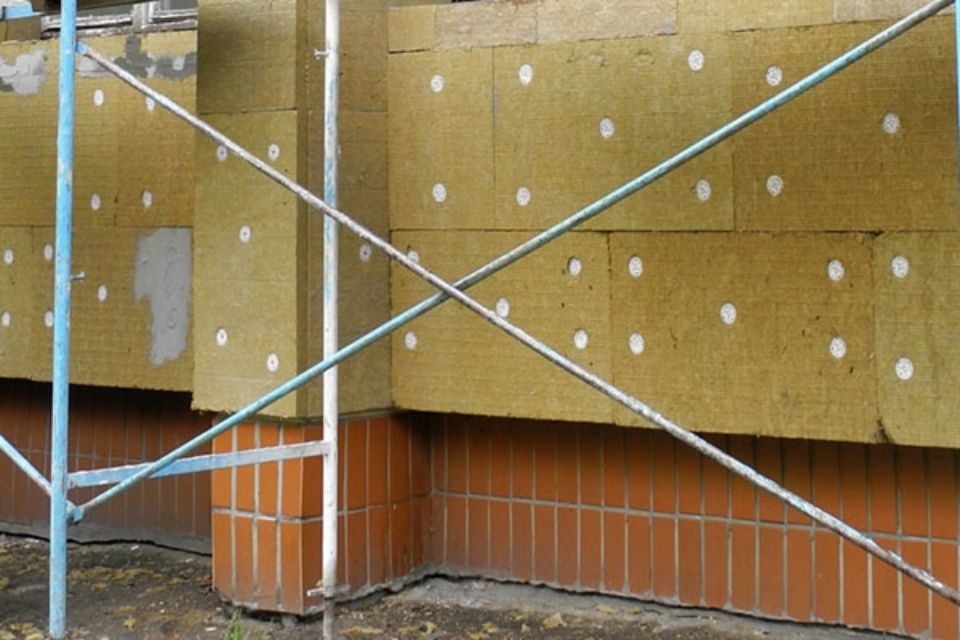 Gerüst vor einer Gebäudewand, die mit gelben Dämmplatten und weißen Befestigungsmitteln verkleidet ist.