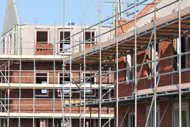 Gerüste um ein im Bau befindliches rotes Backsteingebäude an einem klaren Tag