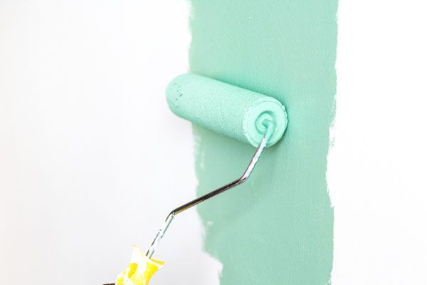 Eine mintgrüne Farbrolle trägt Farbe auf eine weiße Wand auf und erzeugt so einen vertikalen Streifen.