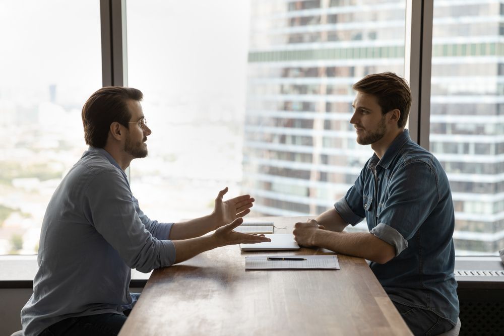 Dos hombres están sentados en una mesa conversando.