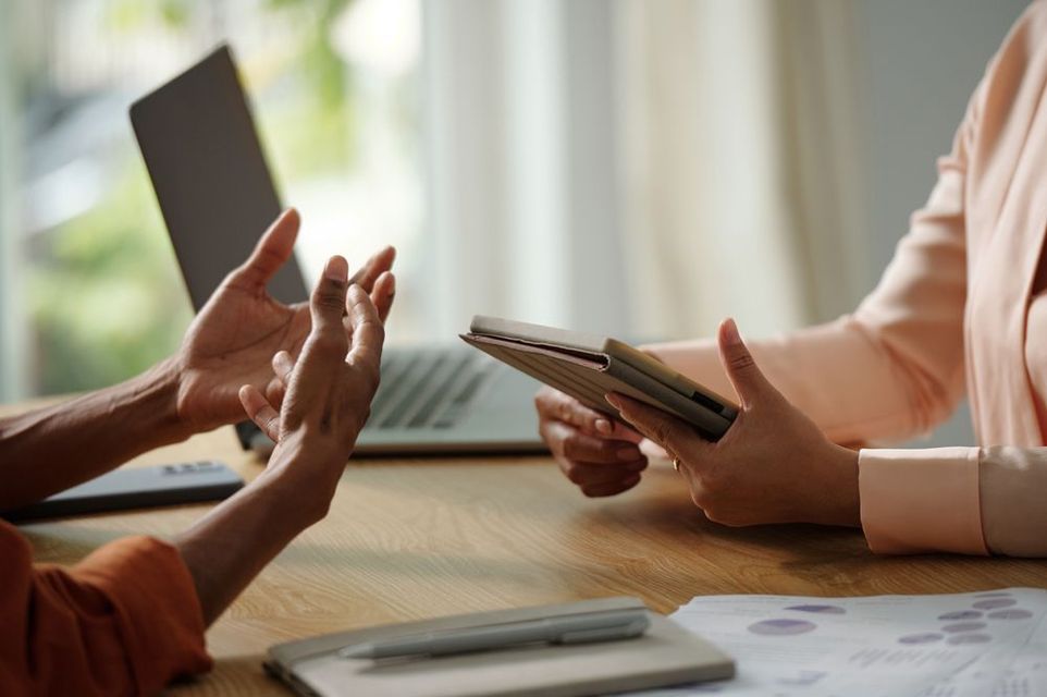 Dos personas están sentadas en una mesa con una computadora portátil y una tableta.