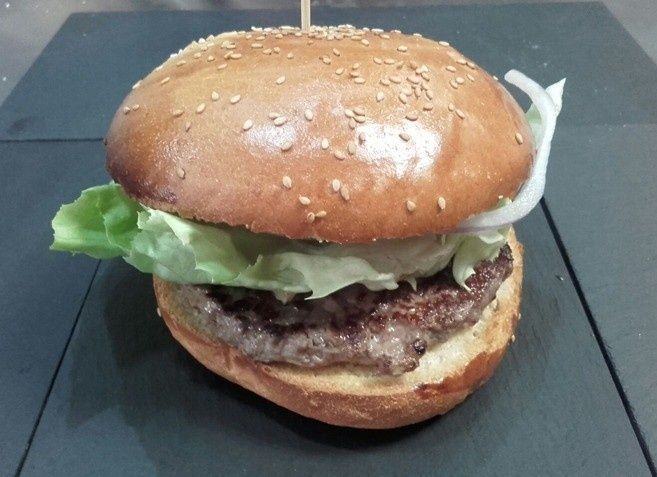 Una hamburguesa con pan de sésamo, lechuga y cebolla en un plato cuadrado oscuro.