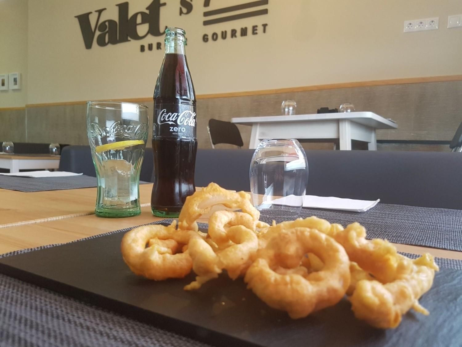 En un restaurante, una bandeja de pizarra con aros de calamar fritos, un vaso de agua con limón y una botella de Coca-Cola.