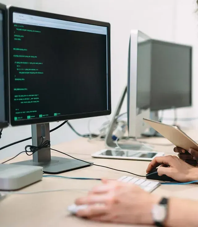 Una persona está escribiendo en un teclado frente a un monitor de computadora.