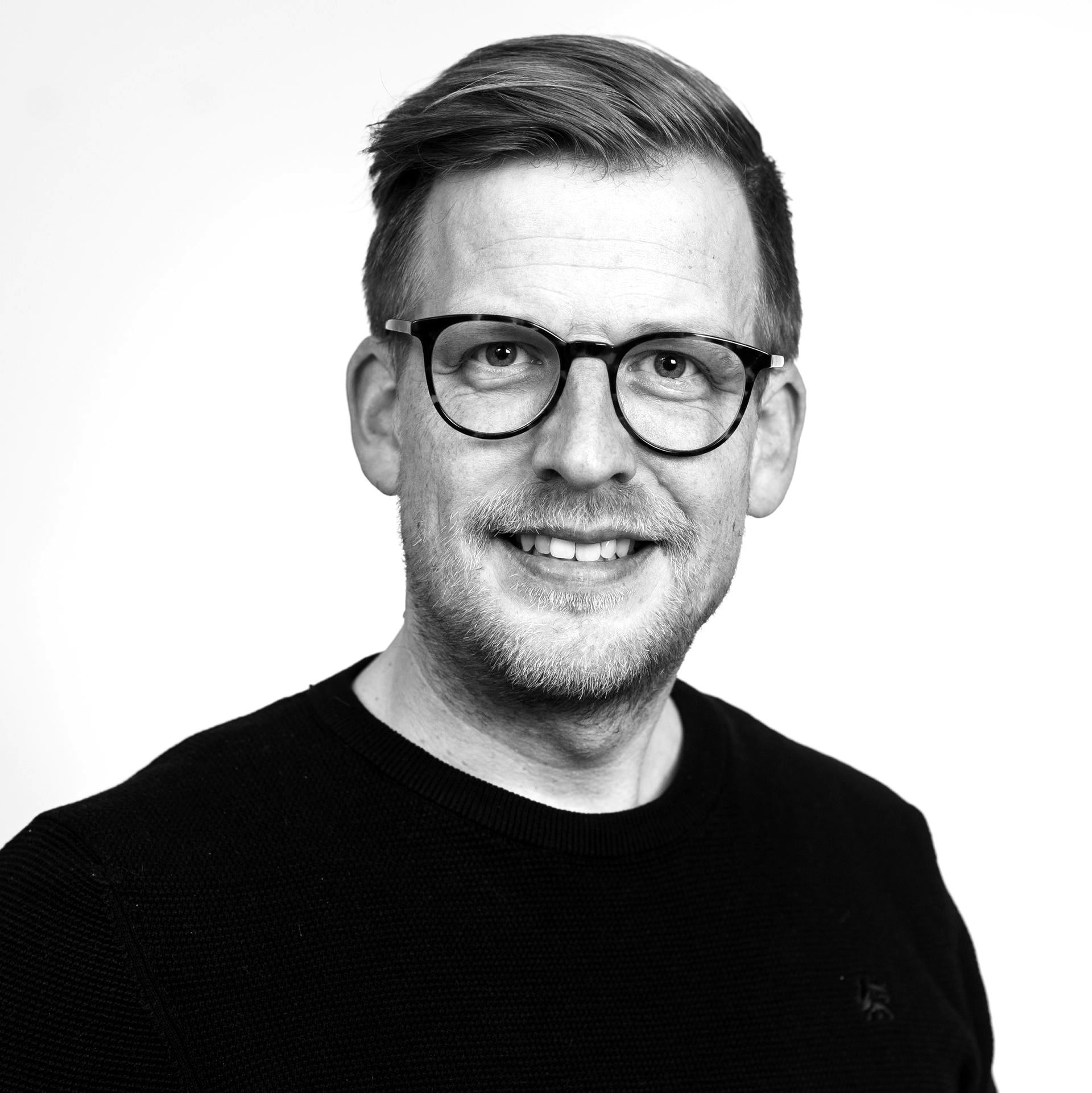 Lächelnde Person mit Brille und schwarzem Hemd vor weißem Hintergrund