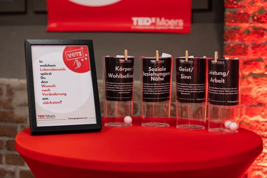 Gerahmte Vitrine auf rotem Tisch mit vier durchsichtigen Auszeichnungstafeln und einem weißen Schild in einem Raum mit Backsteinwänden