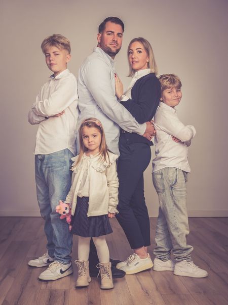 Eine fünfköpfige Familie posiert in aufeinander abgestimmten, hellen Outfits vor einem sanften Studiohintergrund.