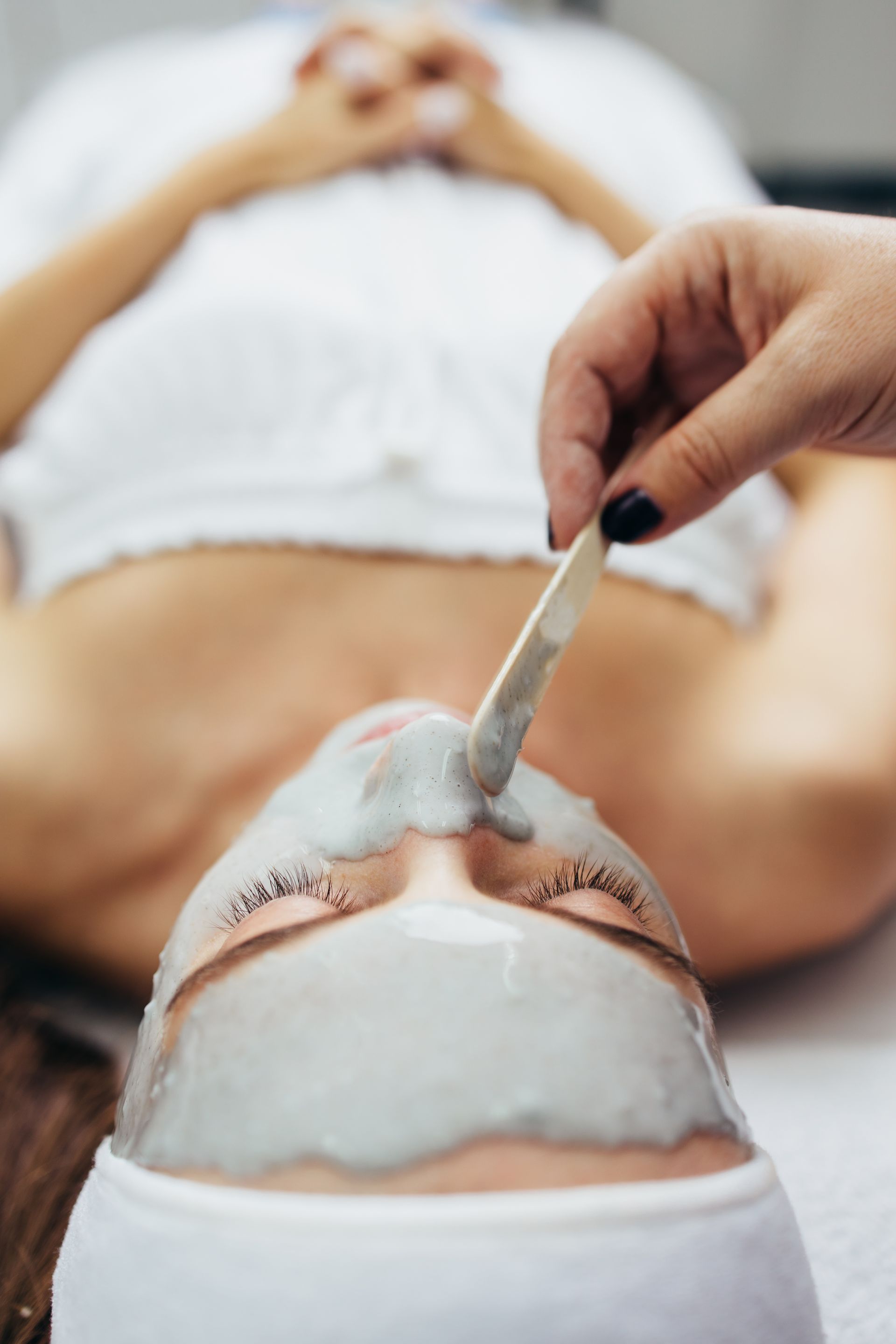 Une personne reçoit un masque facial. Une main applique le masque à l'aide d'une spatule.
