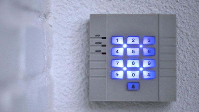 Clavier mural rétroéclairé en bleu à côté d'une porte, avec des touches numérotées et un petit bouton de verrouillage en dessous.