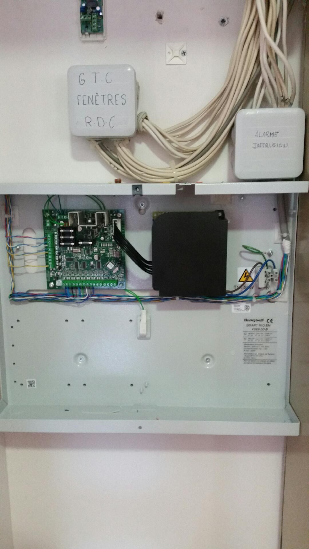 Tableau électrique ouvert avec câblage apparent, circuit imprimé et boîtes de jonction blanches fixées au mur
