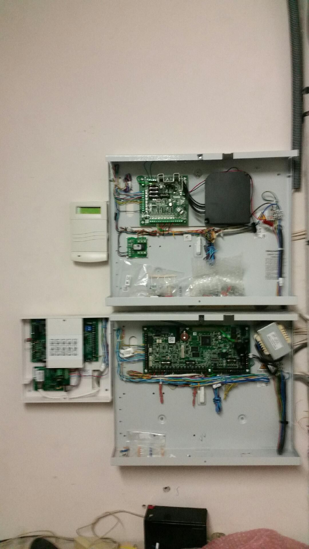 Panneaux de commande muraux ouverts avec circuits imprimés et fils apparents, plus un petit thermostat sur la gauche.