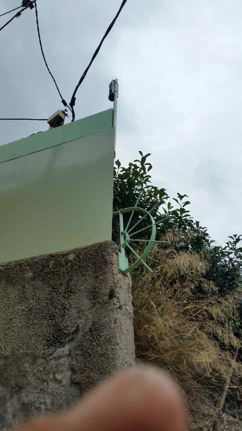 Roue de vélo verte derrière un mur, partiellement cachée par des buissons secs sous un ciel nuageux