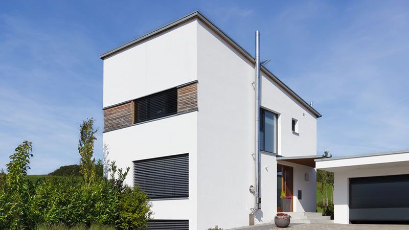 Maison moderne blanche de deux étages avec volets foncés, allée et garage attenant sous un ciel bleu