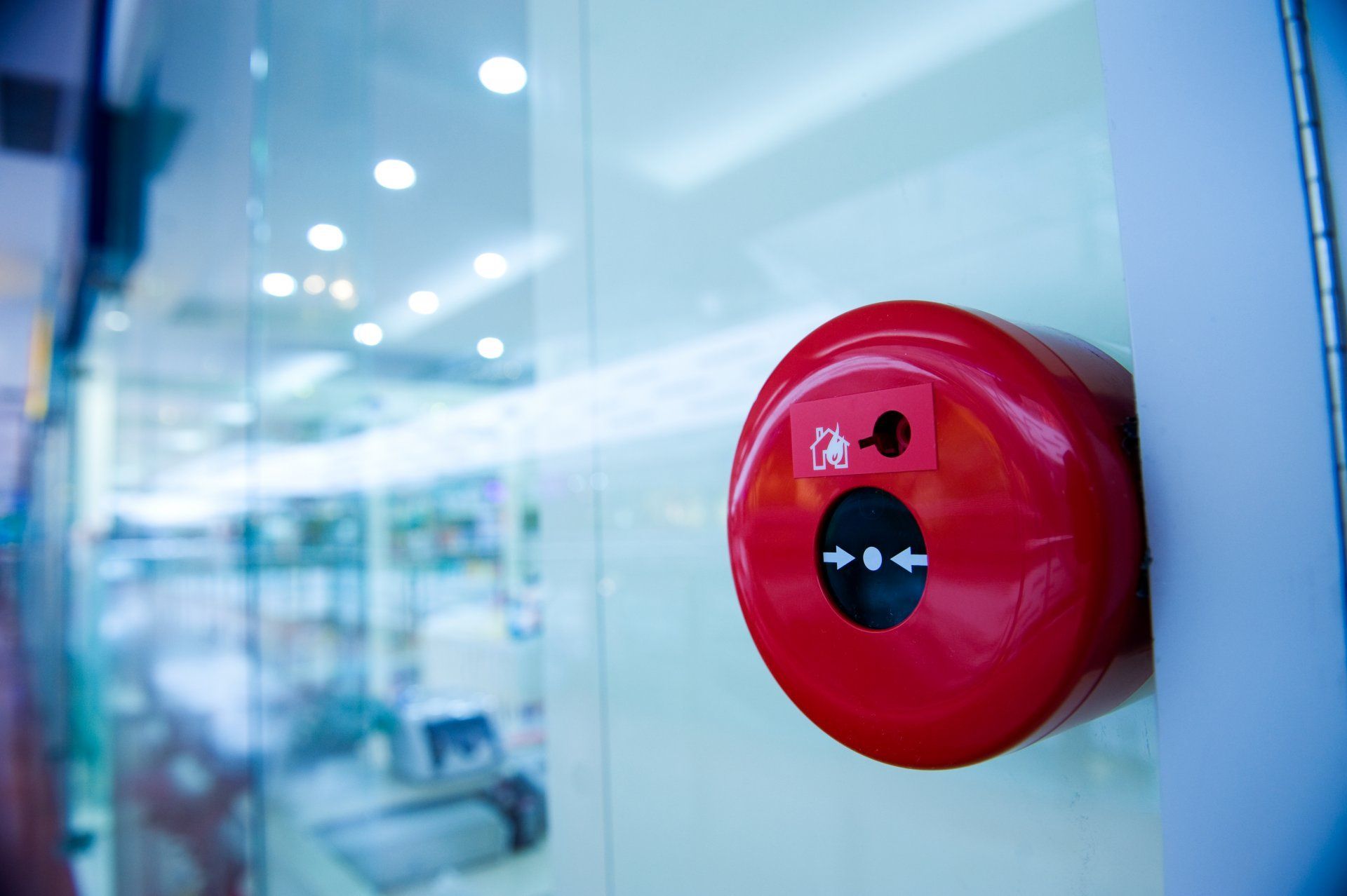Un détecteur de fumée rouge est installé sur une paroi vitrée dans un intérieur de bureau lumineux.