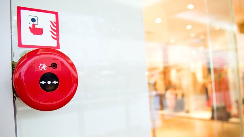 Une alarme incendie rouge sur un mur blanc avec un panneau de sécurité incendie au-dessus.