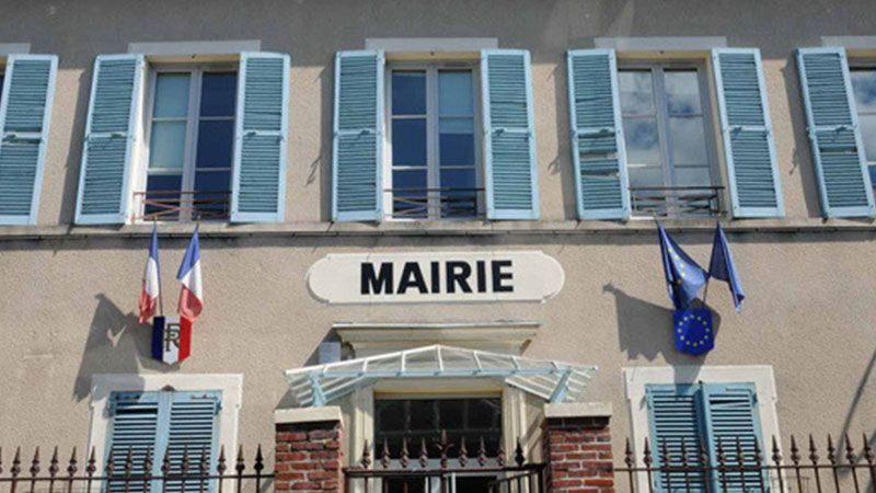 Façade d'une mairie française avec l'enseigne MAIRIE, des volets bleus et des drapeaux au-dessus de l'entrée