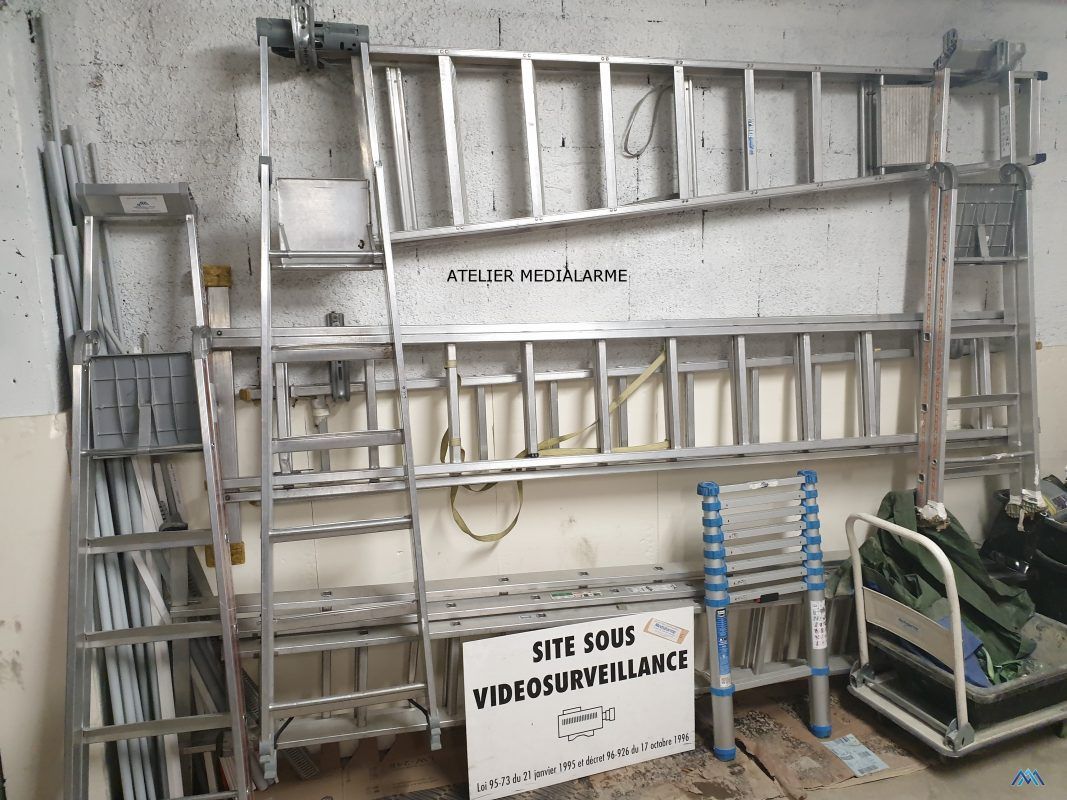 Échafaudages métalliques, échelles et un panneau  dans une zone de stockage.