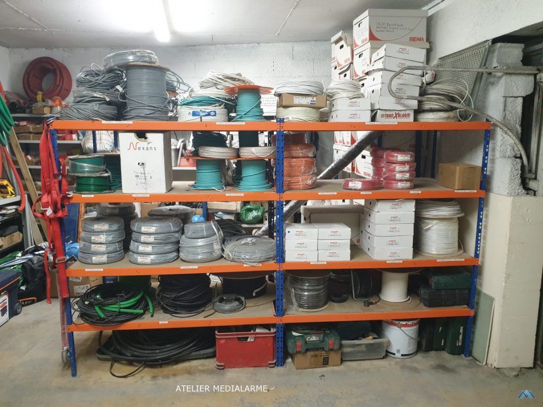 Rayonnages d'entrepôt remplis de pièces en boîte, de câbles enroulés et de bacs dans une salle de stockage encombrée