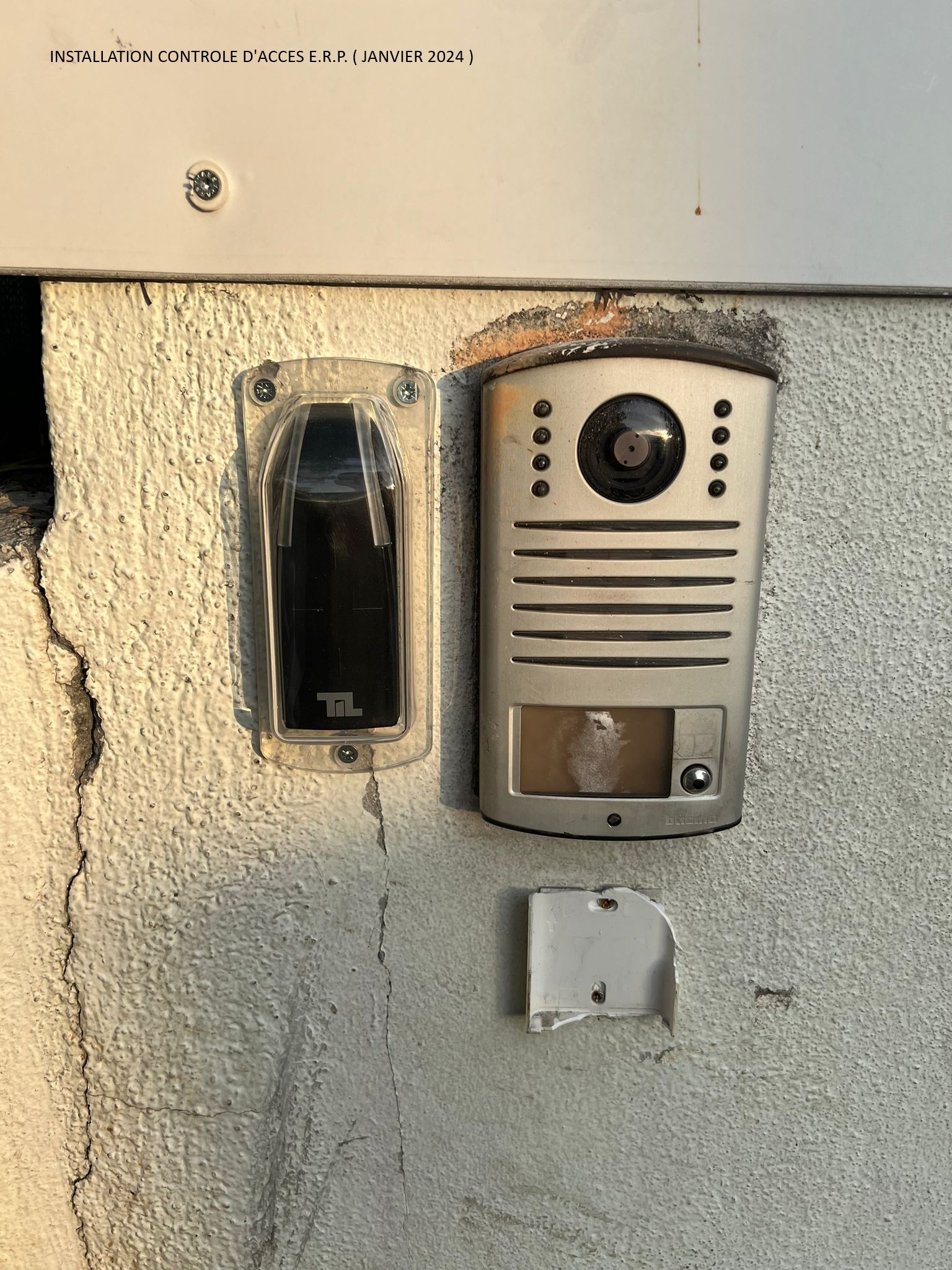 Panneau d'interphone et de sonnette extérieur monté sur un mur en stuc, avec un petit interrupteur blanc en dessous.