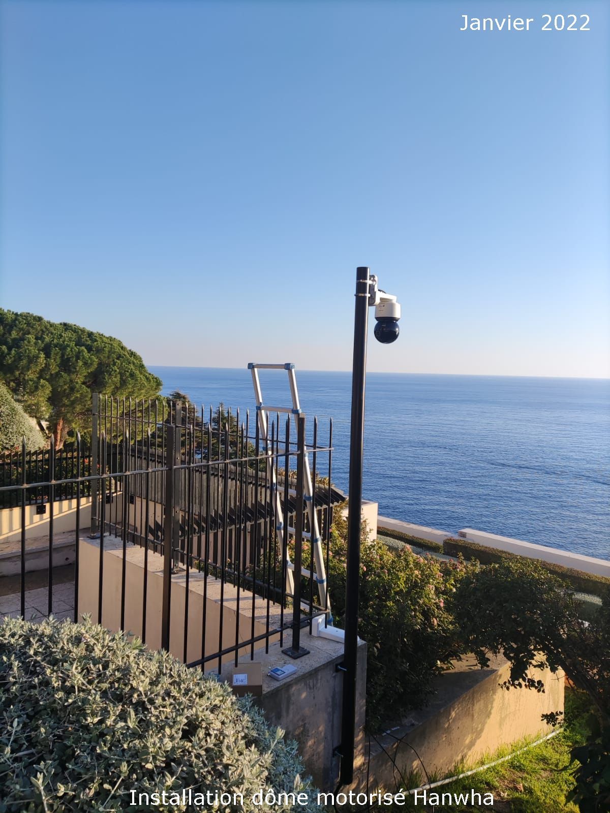 Terrasse en bord de mer avec clôture noire et lampadaire donnant sur un océan bleu calme sous un ciel dégagé