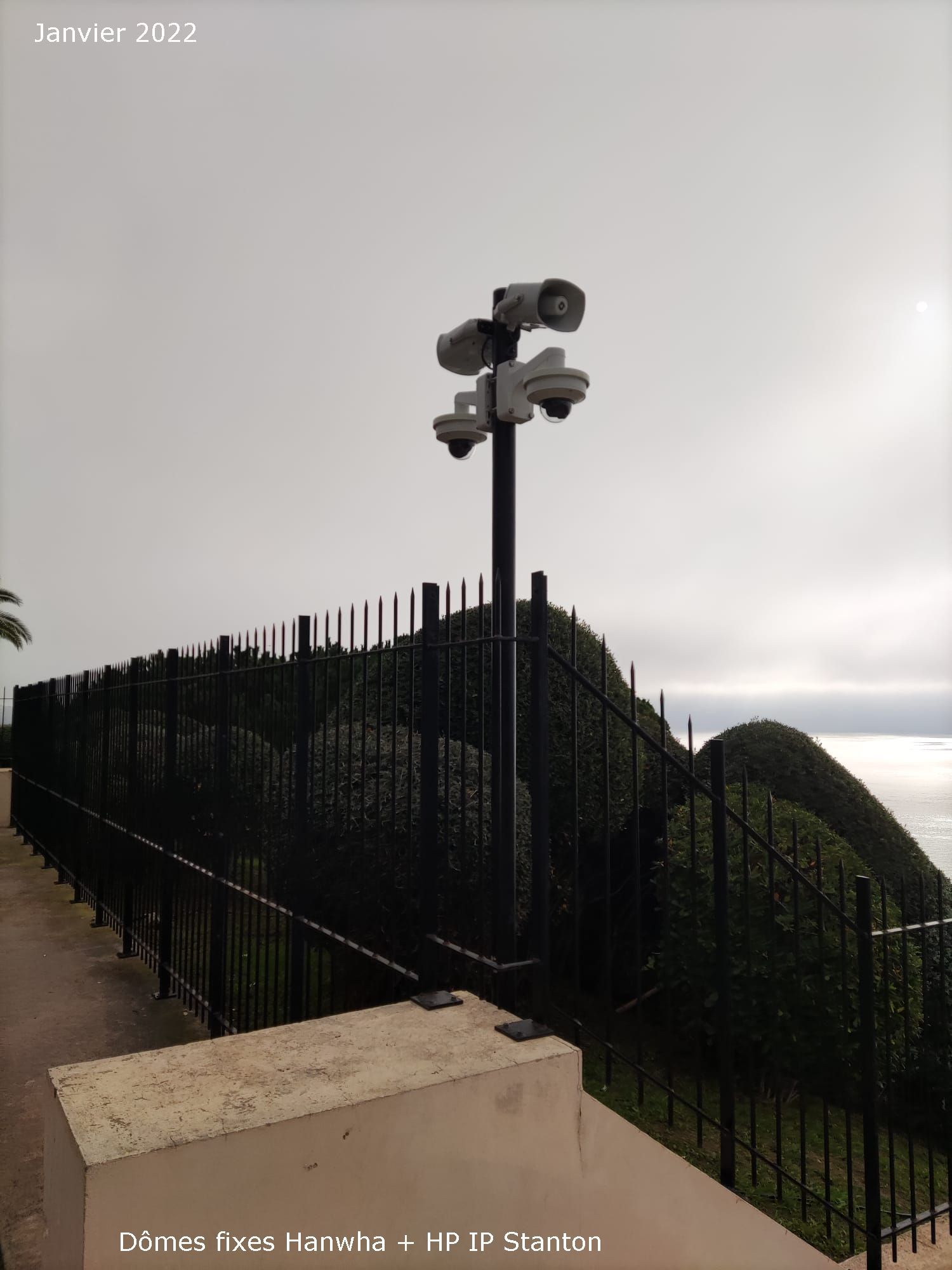 Caméra de sécurité sur le toit, montée sur un poteau au-dessus d'un point de vue clôturé sur une colline, sous un ciel couvert.