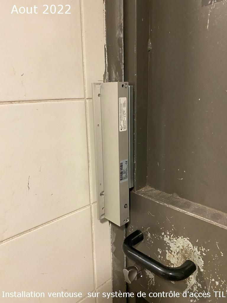 Dispositif de contrôle d'accès mural fixé dans un angle de mur beige, avec étiquettes françaises et câbles apparents.