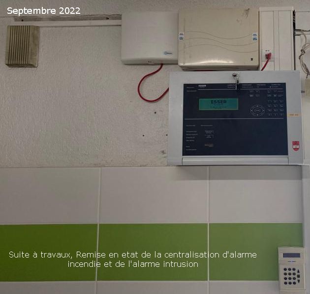 Des panneaux de commande muraux et un clavier numérique dans une pièce, avec un mur carrelé blanc et une bande verte.