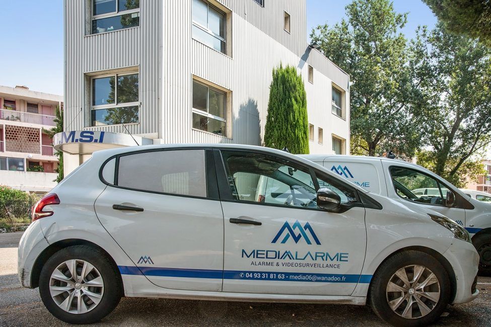 Voiture de service blanche garée devant un bâtiment moderne avec des arbres en arrière-plan