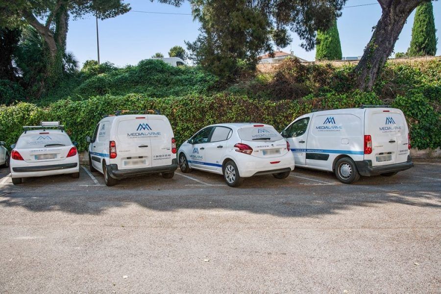 Quatre fourgonnettes de service blanches étaient garées en bord de route, devant d'épaisses haies et des arbres verdoyants.