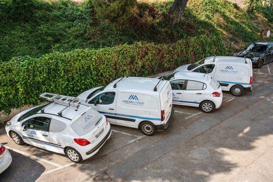 Quatre voitures blanches garées le long d'un trottoir, au bord d'un talus herbeux.