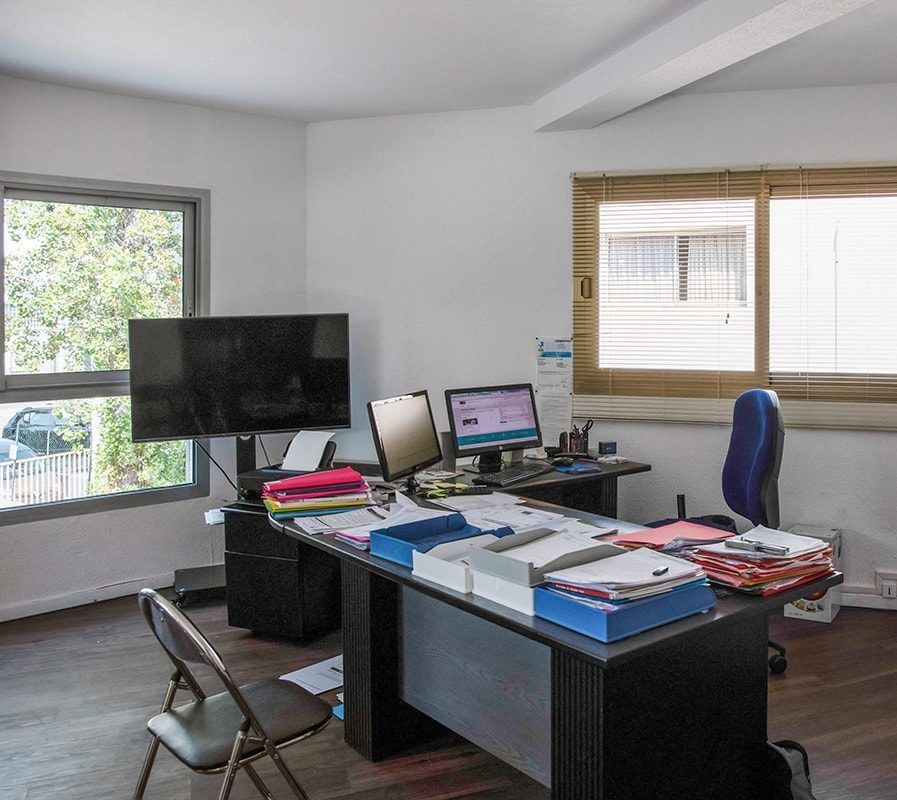 Bureau à domicile avec bureau, écran, chaise et papiers en désordre près d'une fenêtre lumineuse