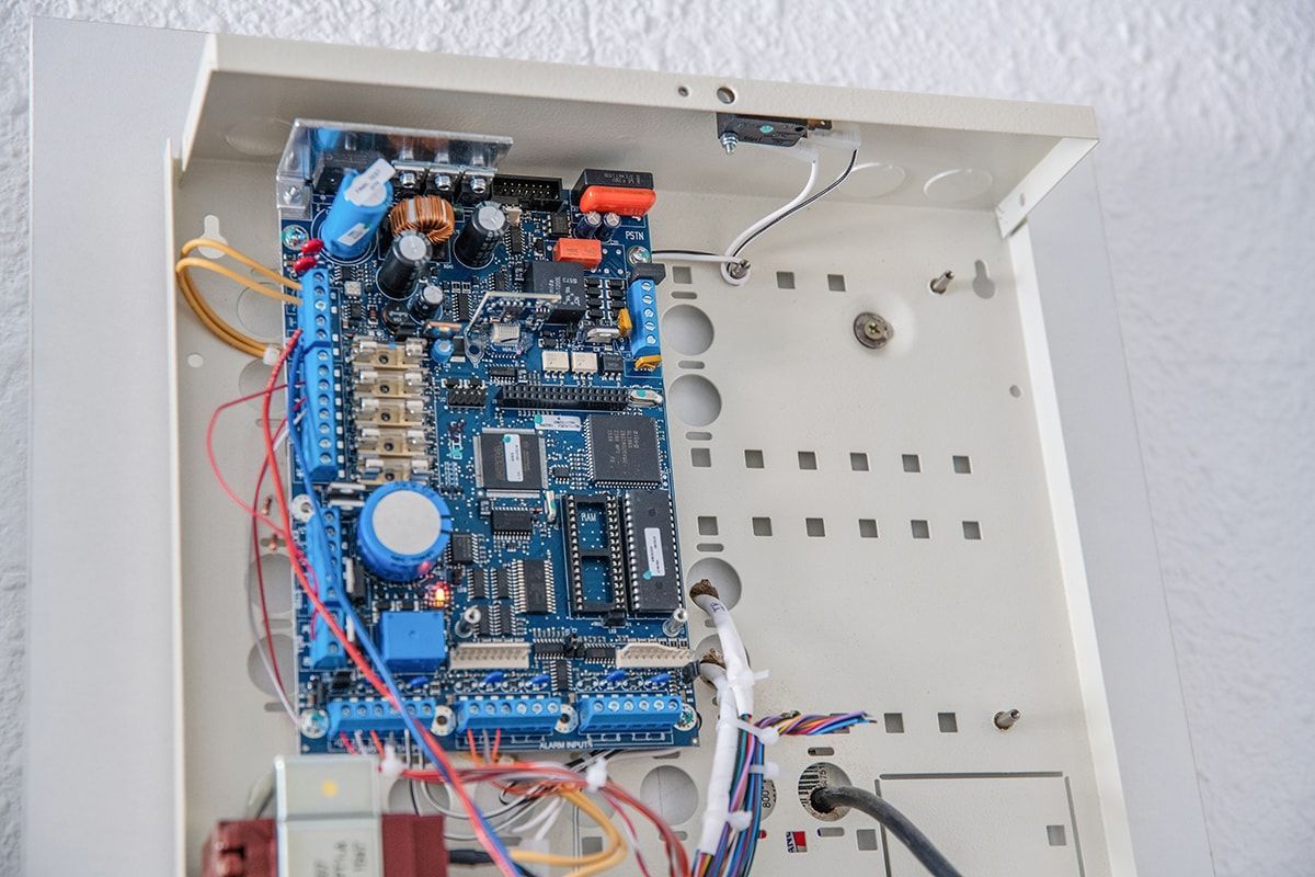 Panneau de commande électrique ouvert avec un circuit imprimé bleu et des câbles à l'intérieur d'un boîtier métallique blanc