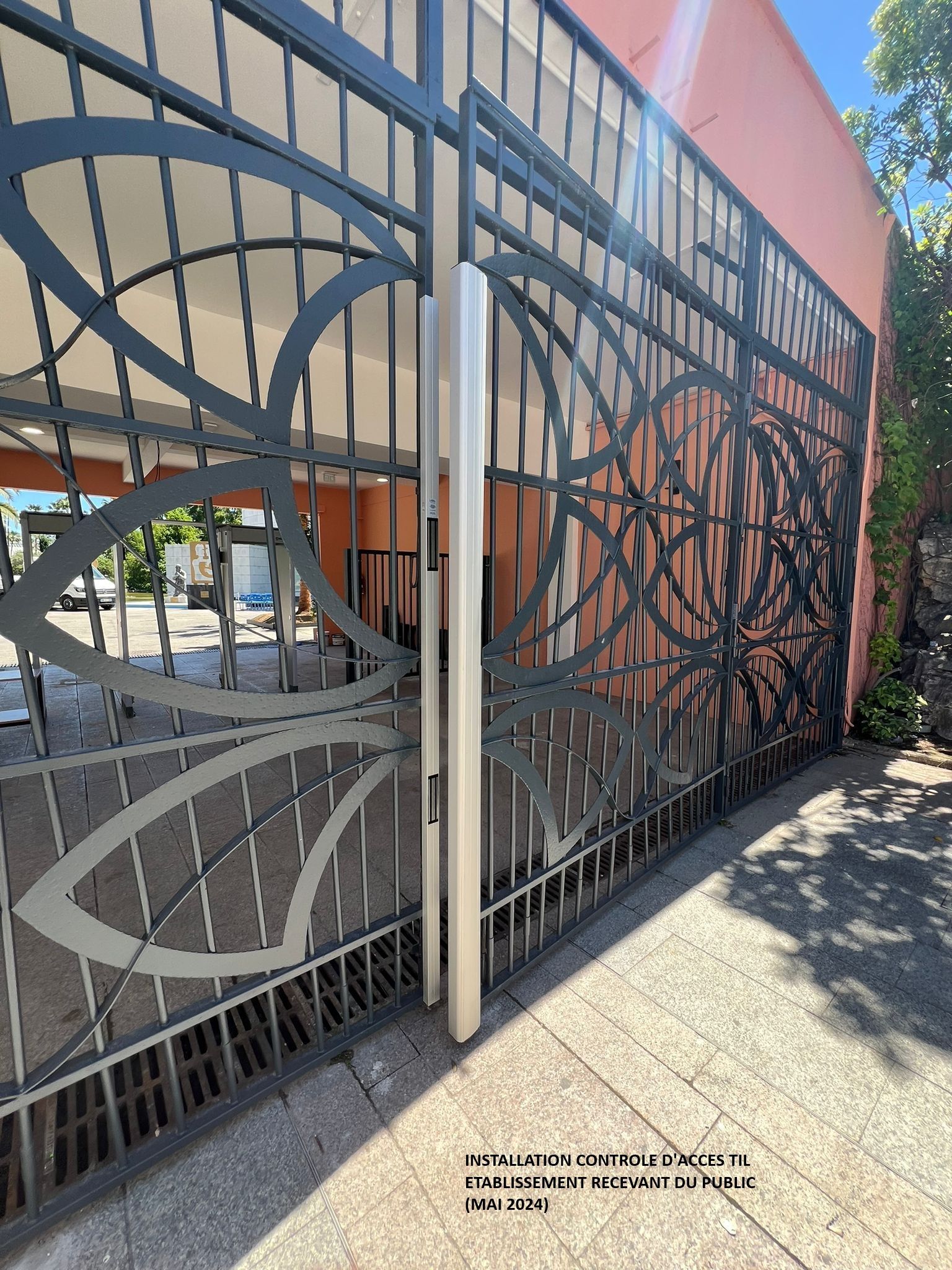 Portail décoratif en métal orné de motifs circulaires abstraits, jouxtant un bâtiment moderne baigné de soleil.