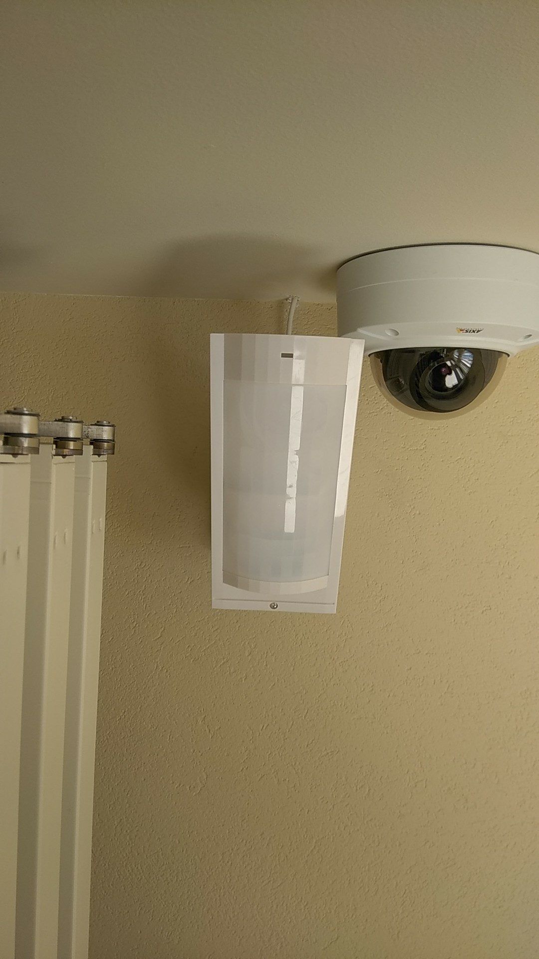Dispositif blanc fixé au mur, à côté d'une caméra de sécurité dôme sur un mur beige.