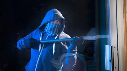 Une personne cagoulée pointe un fusil long à travers une porte dans une pénombre bleue.