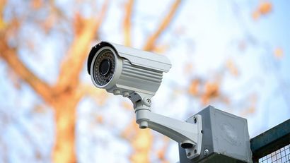 Caméra de sécurité grise installée à l'extérieur, se détachant sur un fond d'arbres et de ciel d'automne flous.