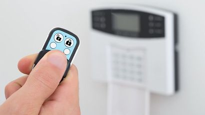 Main tenant une petite télécommande pointée vers un clavier d'alarme de sécurité mural