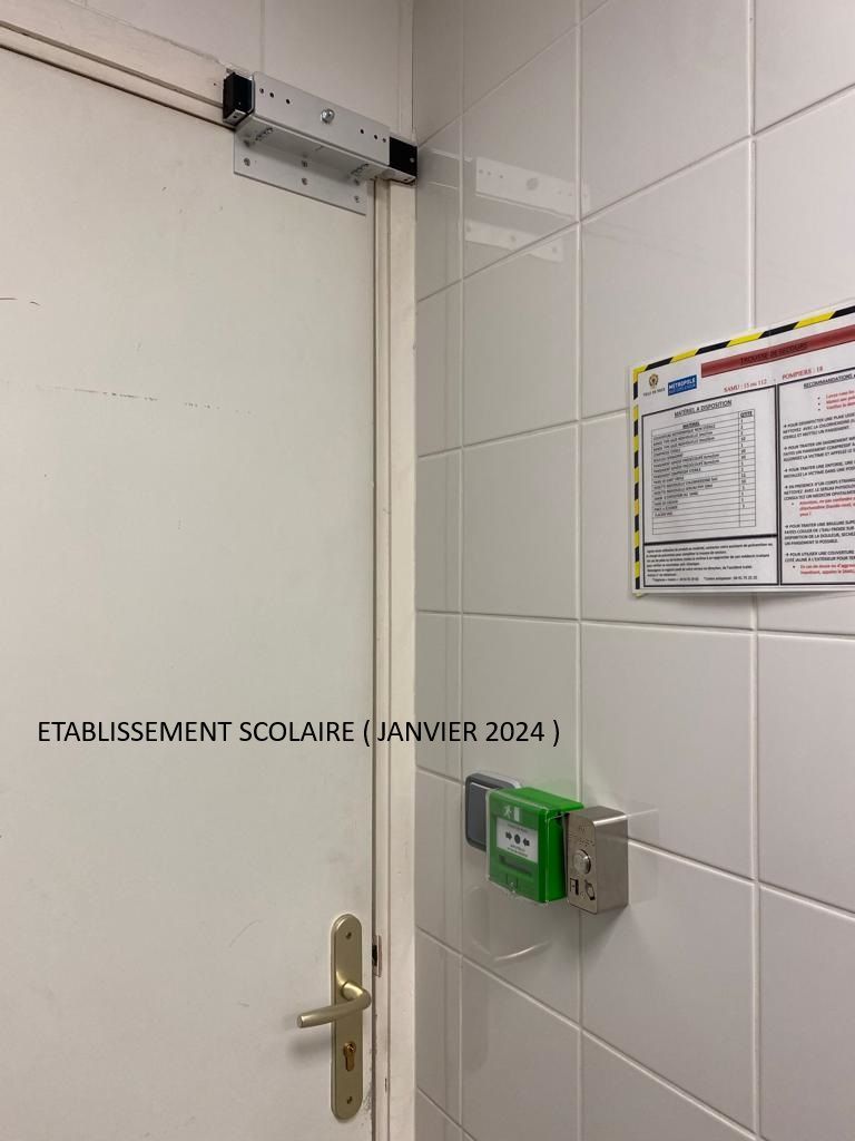 Porte intérieure blanche avec un dispositif d'accès mural vert et un avis affiché dans un couloir carrelé