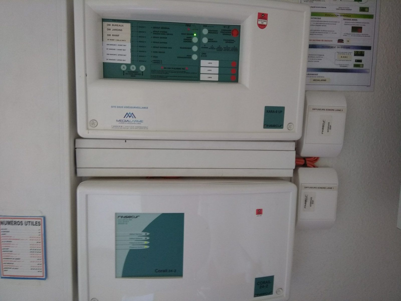 Deux panneaux de commande blancs fixés au mur, avec étiquettes et voyants lumineux.