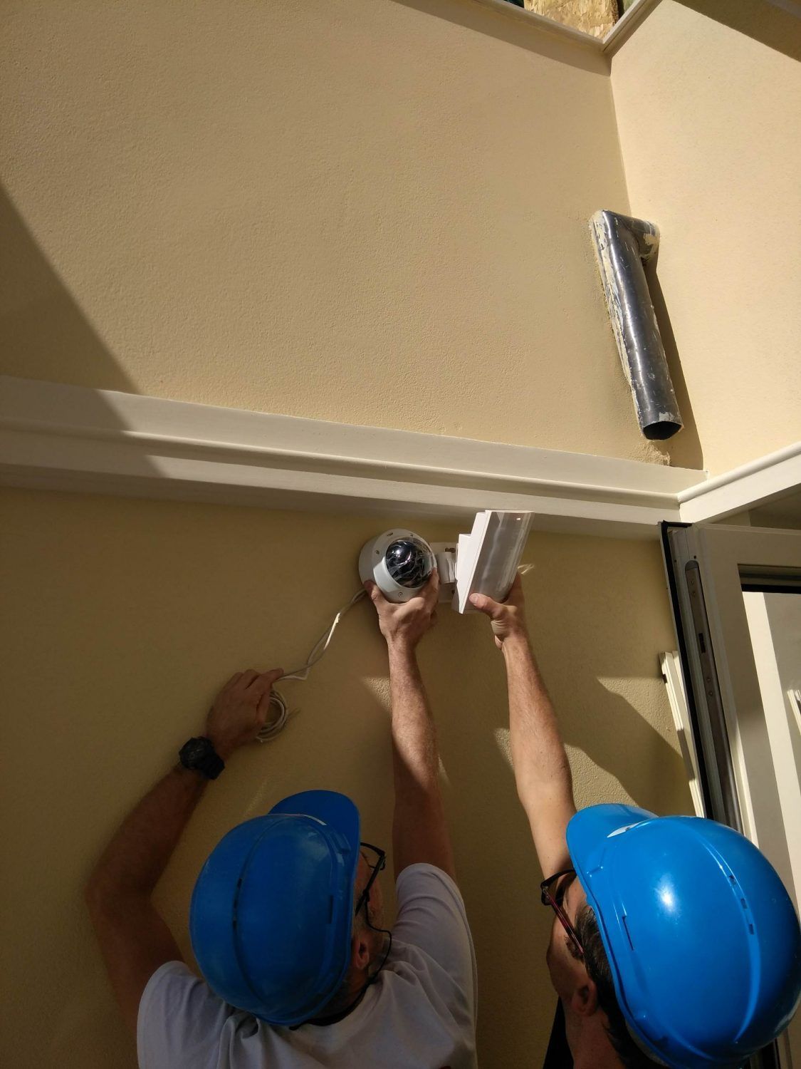 Deux ouvriers portant des casques de chantier bleus utilisent des outils sur un mur extérieur en construction.