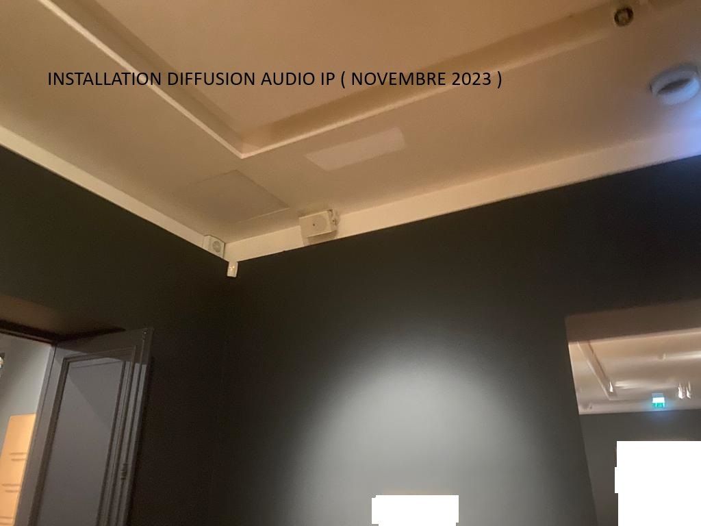 Plafond sombre de la galerie avec éclairage sur rail mural et un projecteur lumineux sur un mur noir.