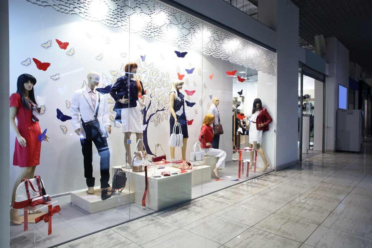 Des mannequins, exposés dans la vitrine éclairée d'un magasin de vêtements, présentent des tenues rouges, blanches et bleues.