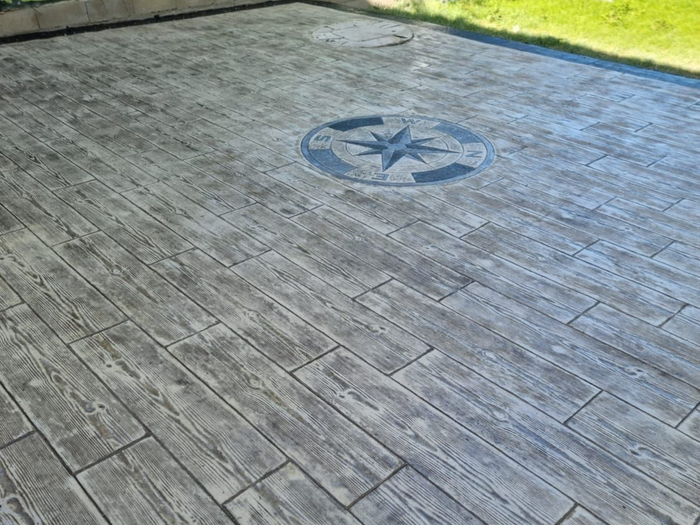Vers la page Béton imprimé. Une terrasse attenante à un jardin en béton imprimé de couleur grise et une rose des vents.